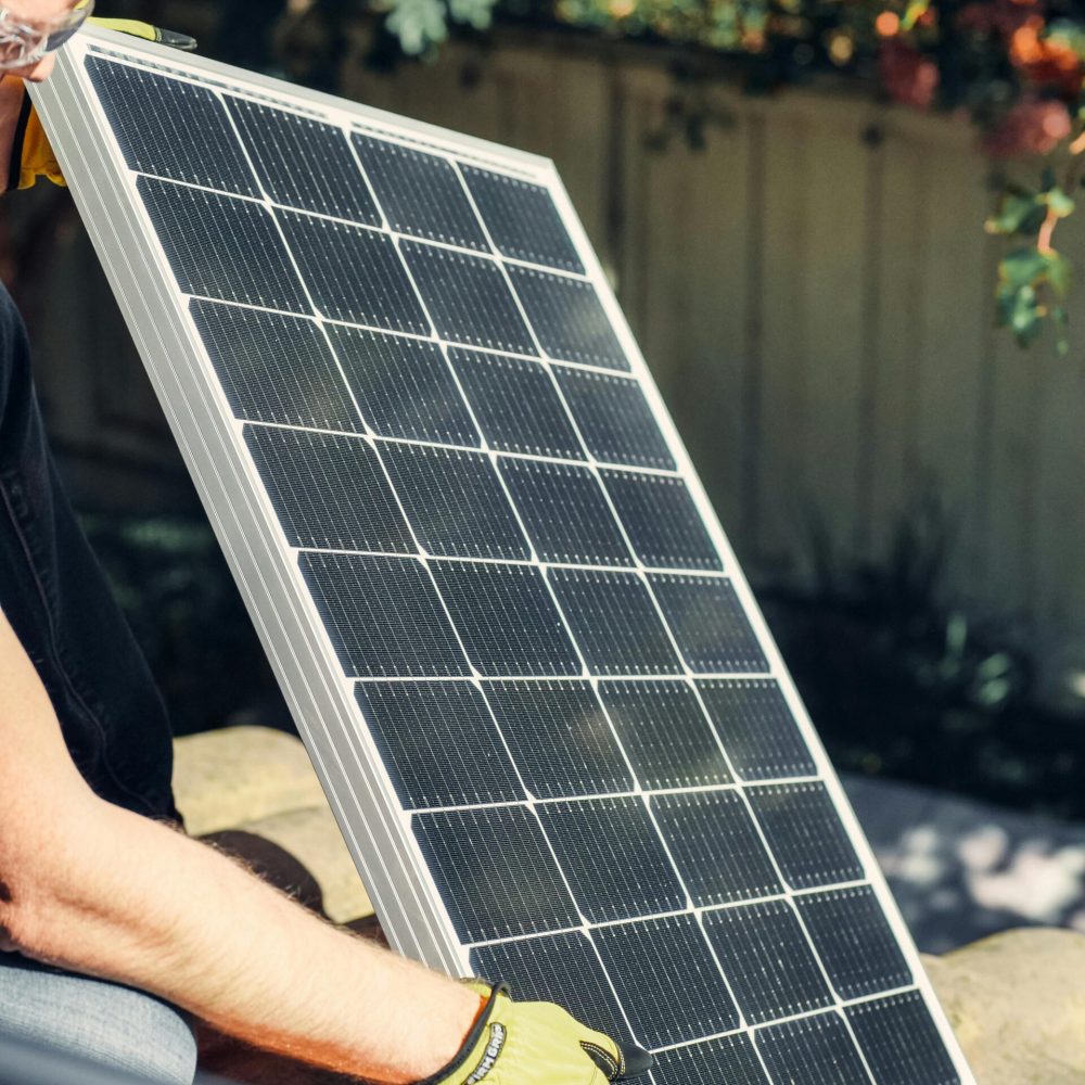A worker installs a solar panel in a garden, promoting clean energy.